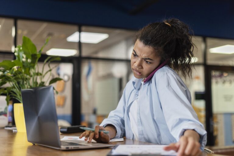 stressed-woman-office-using-laptop-talking-smartphone